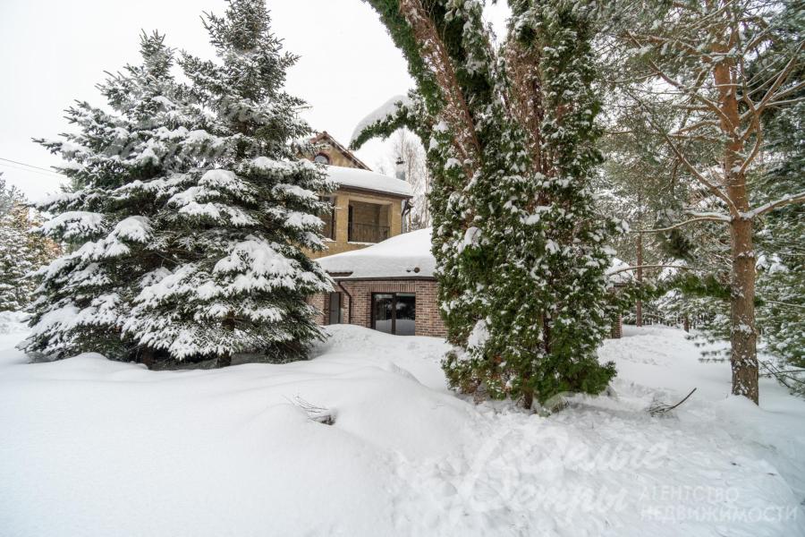 Дом стоит на живописном участке с хвойными деревьями, кустарниками, клумбами, газоном