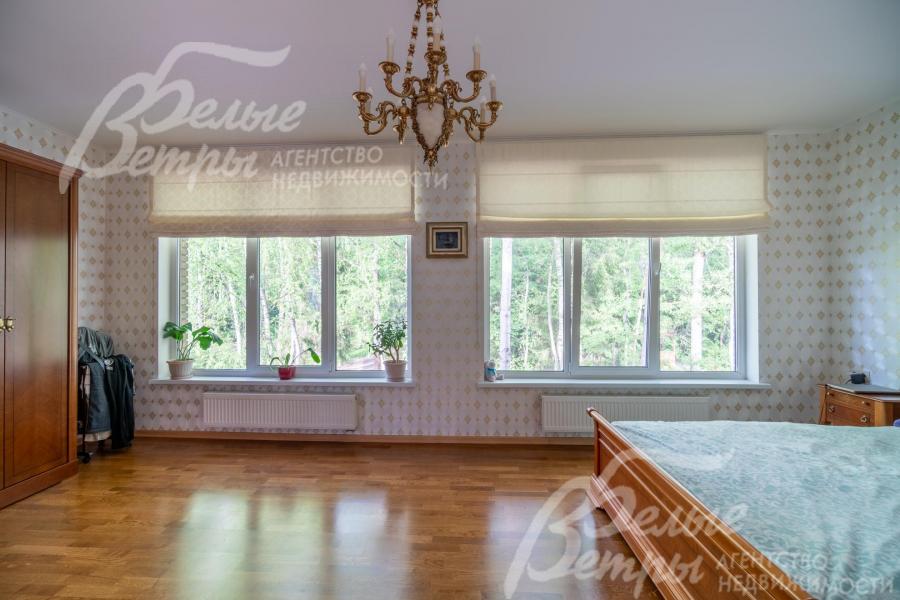 Главная спальня с двумя большими окнами с видом на лес украшена дорогостоящей люстрой