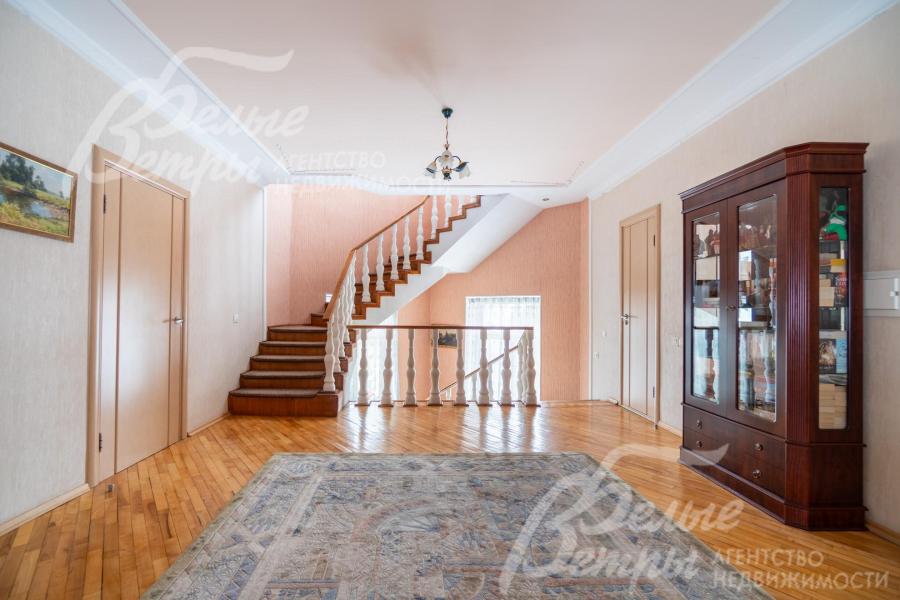 Просторный холл второго этажа: на полу - паркет, справа располагается шкаф-витрина из тёмного дерева в классическом стиле