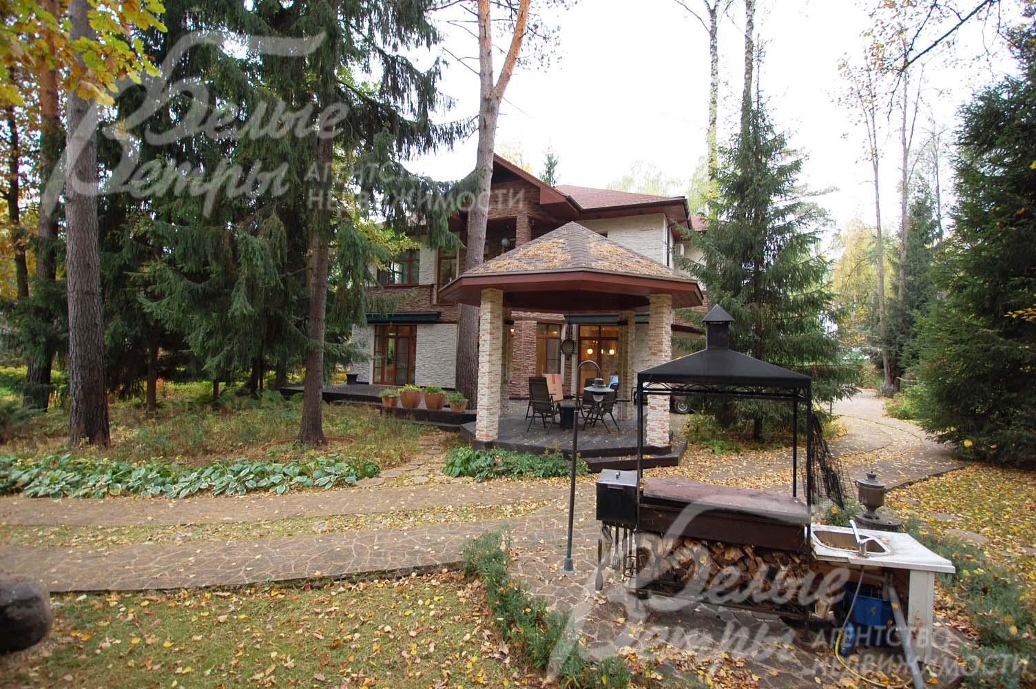 Около дома уютная беседка, неподалеку от нее мангал с элементами летней кухни