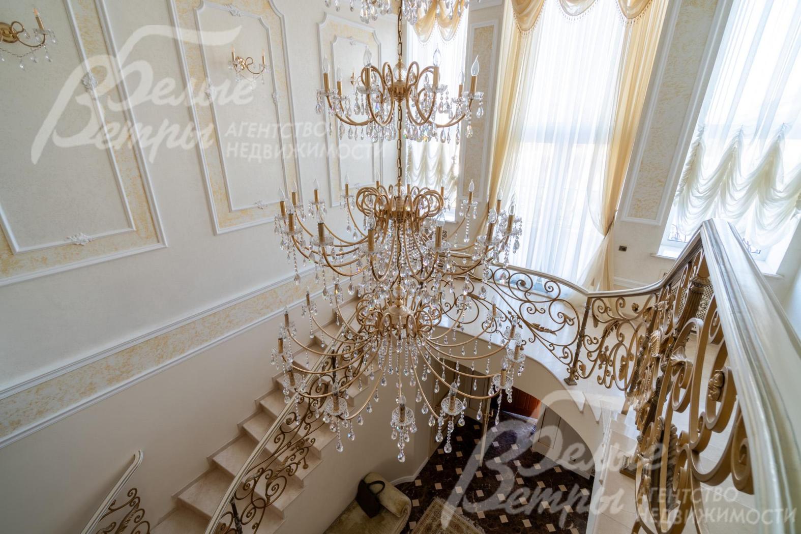 Вид с лестничного марша на первый этаж: над лестничным холлом висит пятиярусная итальянская хрустальная люстра высотой 4 м на 52 лампы