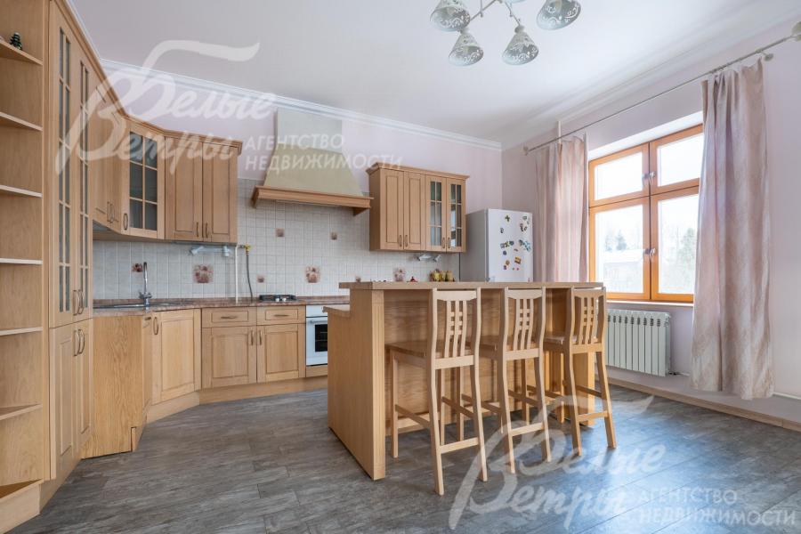 На кухне установлен гарнитур из массива дерева с единой каменной столешницей и барной стойкой