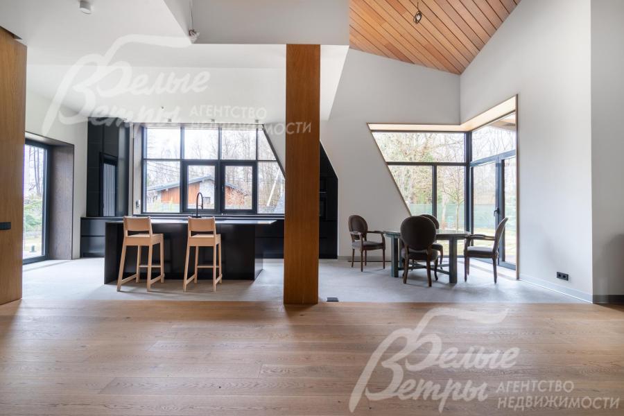 Совмещённая зона кухни, столовой и гостиной - с панорамным остеклением: большие окна и нестандартные треугольные проёмы создают ощущение открытого пространства и связи с лесом