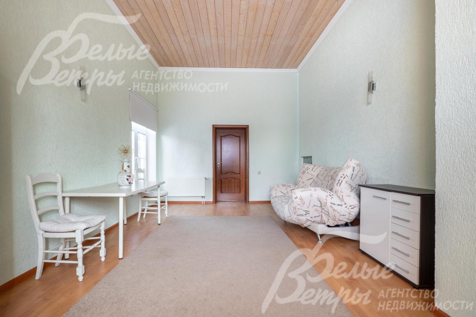 У стены расположен раскладной диван и комод, есть стол с двумя стульями, потолок оформлен деревянными панелями