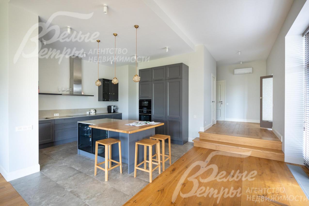 Кухня с гарнитуром и островом отделена от пространства гостиной-столовой контрастным полом и стенами без дверей