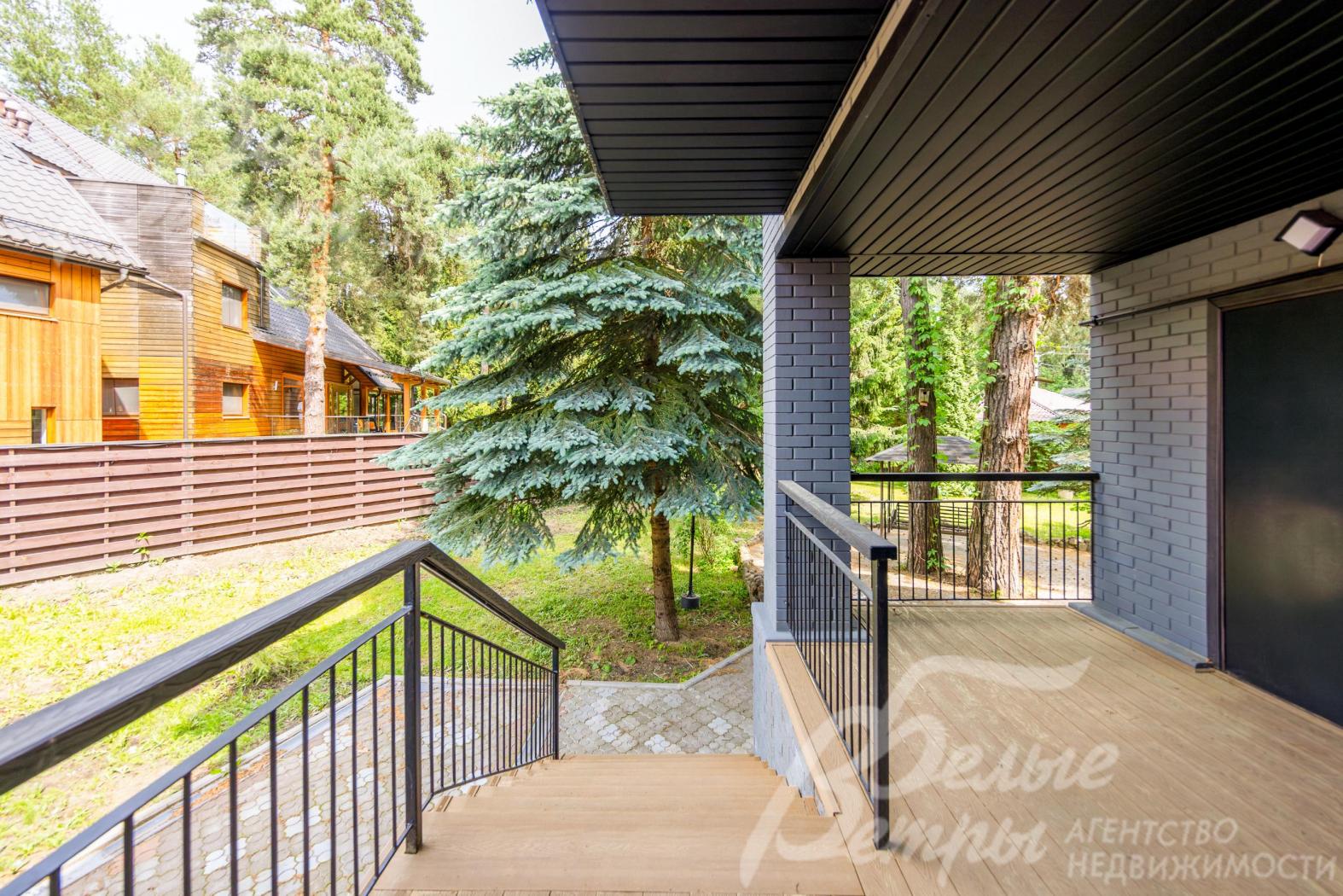 Возле главного входа в дом - уютная крытая терраса с лестницей, спускающейся на участок