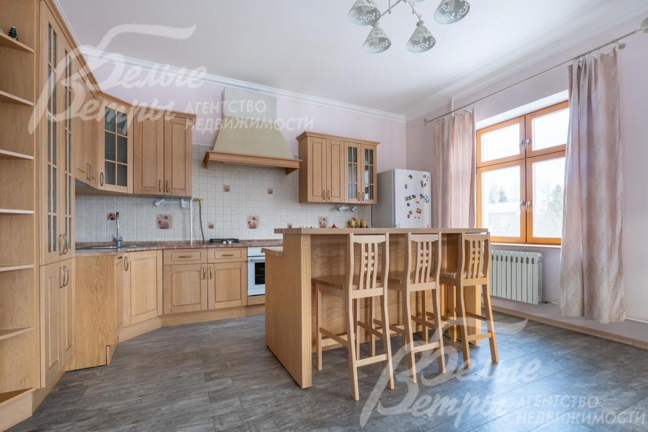 На кухне установлен гарнитур из массива дерева с единой каменной столешницей и барной стойкой