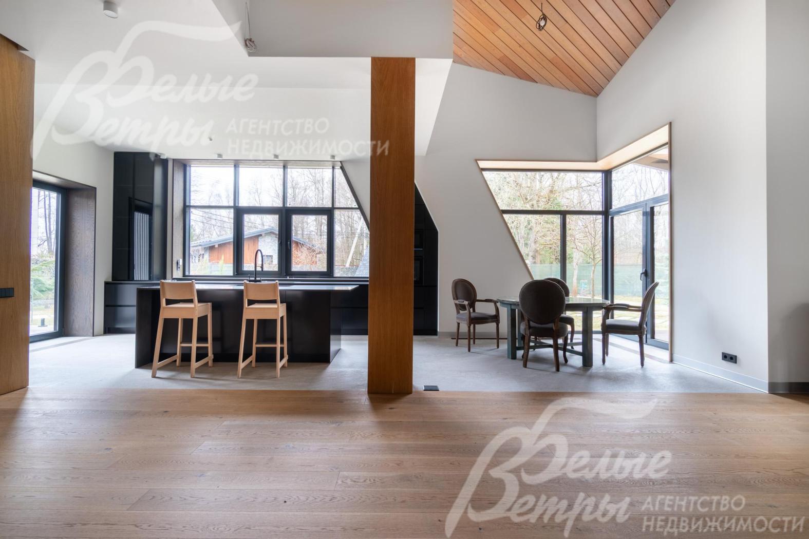 Совмещённая зона кухни, столовой и гостиной - с панорамным остеклением: большие окна и нестандартные треугольные проёмы создают ощущение открытого пространства и связи с лесом