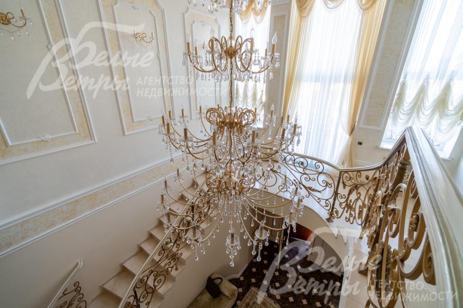 Вид с лестничного марша на первый этаж: над лестничным холлом висит пятиярусная итальянская хрустальная люстра высотой 4 м на 52 лампы